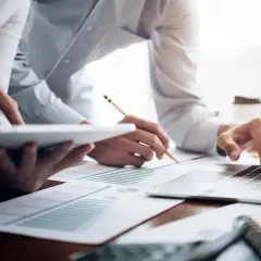 Dwie osoby pracujące przy biurku z laptopem, tabletem i dokumentami.
